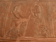 Szene 4.2: Krieger mit Spitzbart und Schwertgehänge unter dem Arm, mit senkrecht in der rechten Hand gehaltenen Schwert, fasst mit der Linken den Arm einer Frau in Prachtgewand. Menelaos und Helena?
